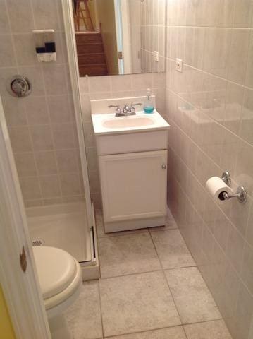 bathroom featuring vanity, toilet, tile walls, a stall shower, and tile patterned floors
