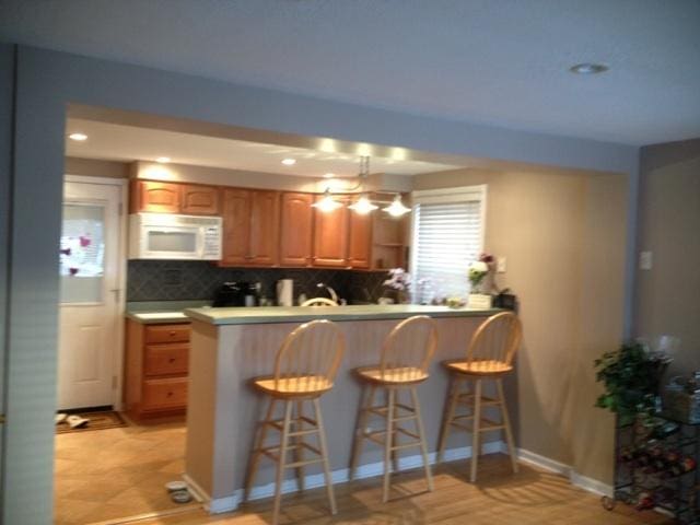 kitchen with a kitchen breakfast bar, recessed lighting, white microwave, a peninsula, and backsplash