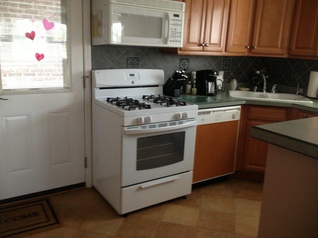 kitchen with a sink, backsplash, brown cabinetry, and white appliances