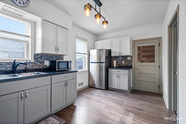 kitchen with dark countertops, a sink, stainless steel appliances, decorative backsplash, and visible vents
