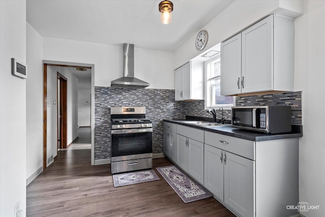 kitchen featuring wall chimney range hood, backsplash, appliances with stainless steel finishes, dark countertops, and a sink