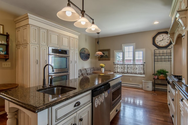 kitchen featuring a sink, appliances with stainless steel finishes, baseboard heating, cream cabinets, and a kitchen island with sink