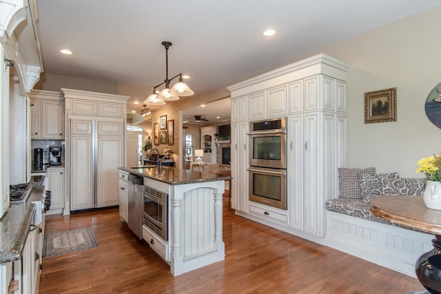 kitchen featuring dark stone counters, a ceiling fan, wood finished floors, and stainless steel appliances