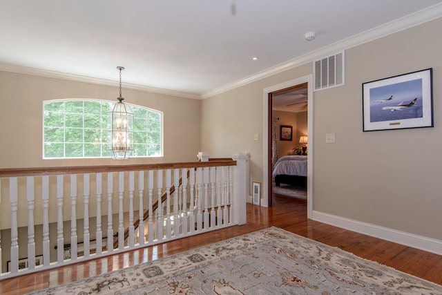 hallway featuring visible vents, baseboards, an inviting chandelier, ornamental molding, and wood finished floors