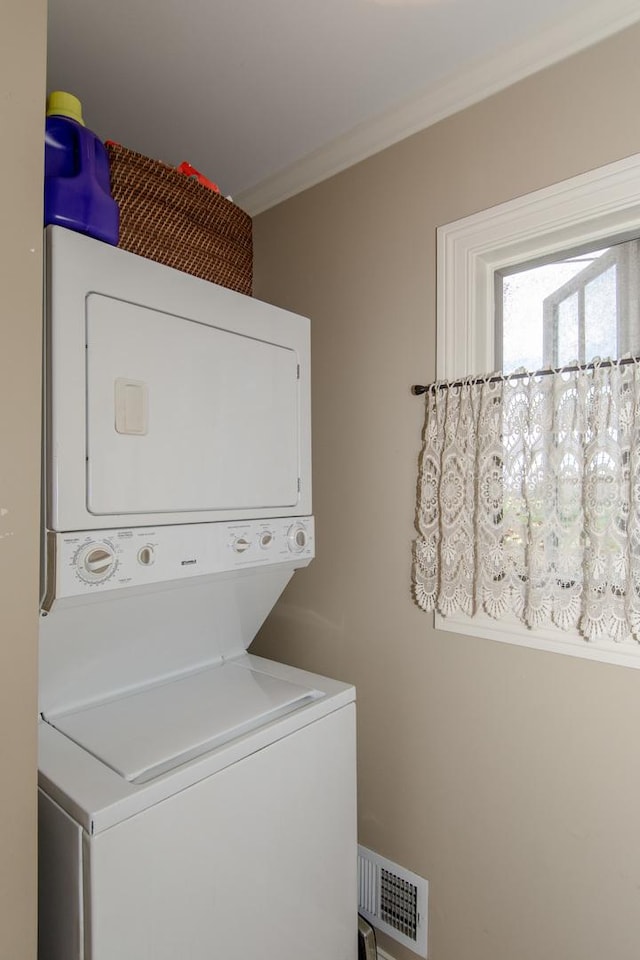 laundry area with crown molding, visible vents, stacked washing maching and dryer, and laundry area