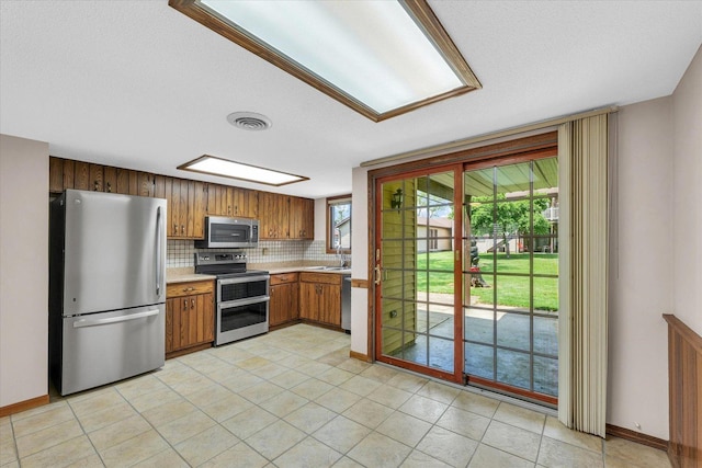 kitchen with stainless steel appliances, light countertops, tasteful backsplash, brown cabinetry, and plenty of natural light