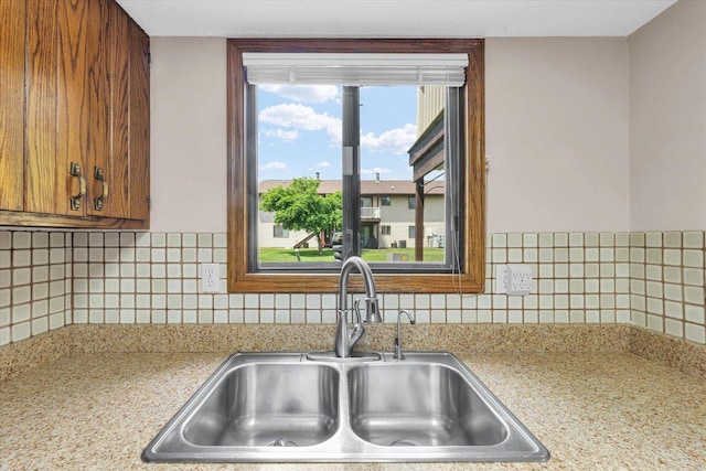 kitchen with a sink, light countertops, brown cabinets, and backsplash