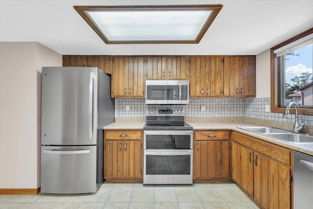 kitchen featuring appliances with stainless steel finishes, a sink, brown cabinets, and light countertops