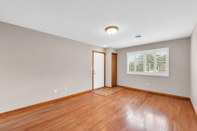 unfurnished room featuring baseboards, light wood-style floors, and a textured ceiling