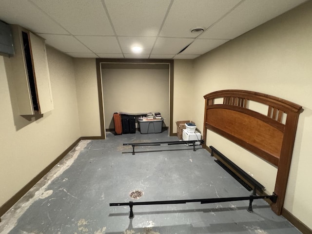 bedroom featuring concrete flooring, a drop ceiling, and baseboards
