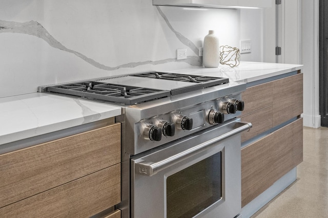 details with modern cabinets, brown cabinetry, high end stove, and light stone countertops