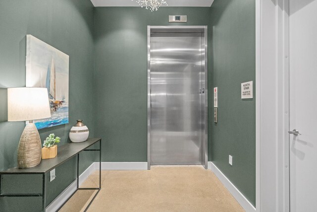 hall with a chandelier, elevator, and baseboards