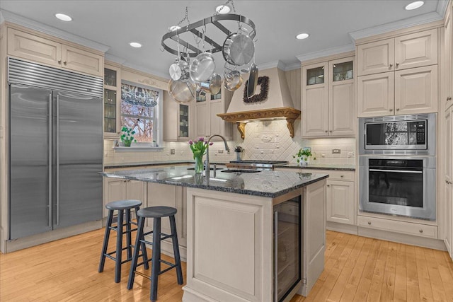kitchen with beverage cooler, built in appliances, light wood-type flooring, and a sink