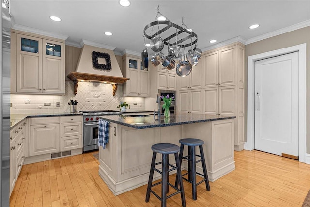 kitchen with light wood-style flooring, visible vents, decorative backsplash, stainless steel stove, and premium range hood