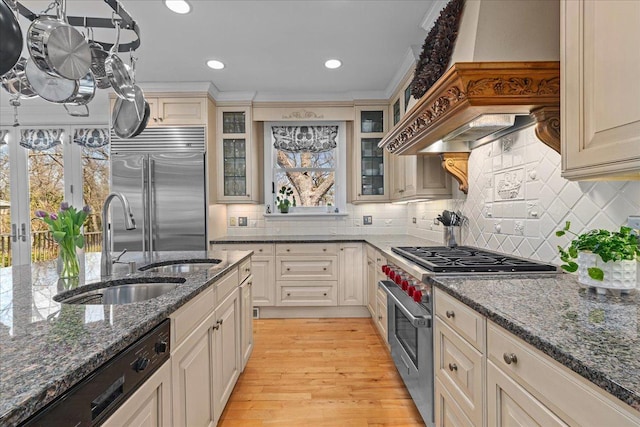 kitchen featuring high end appliances, premium range hood, dark stone counters, decorative backsplash, and light wood-style flooring