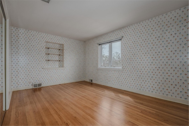 empty room with baseboards, wallpapered walls, visible vents, and light wood-style flooring