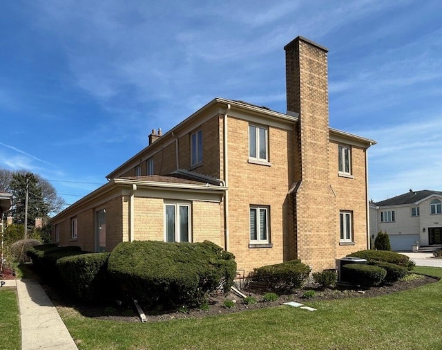 view of home's exterior with brick siding, a yard, and a chimney