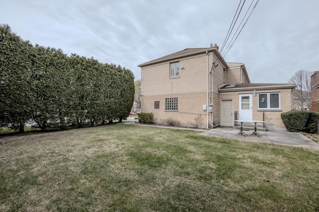 back of property featuring a chimney, a shingled roof, a yard, a patio, and brick siding