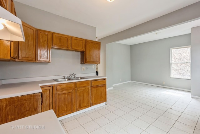 kitchen with a sink, brown cabinets, light countertops, and under cabinet range hood
