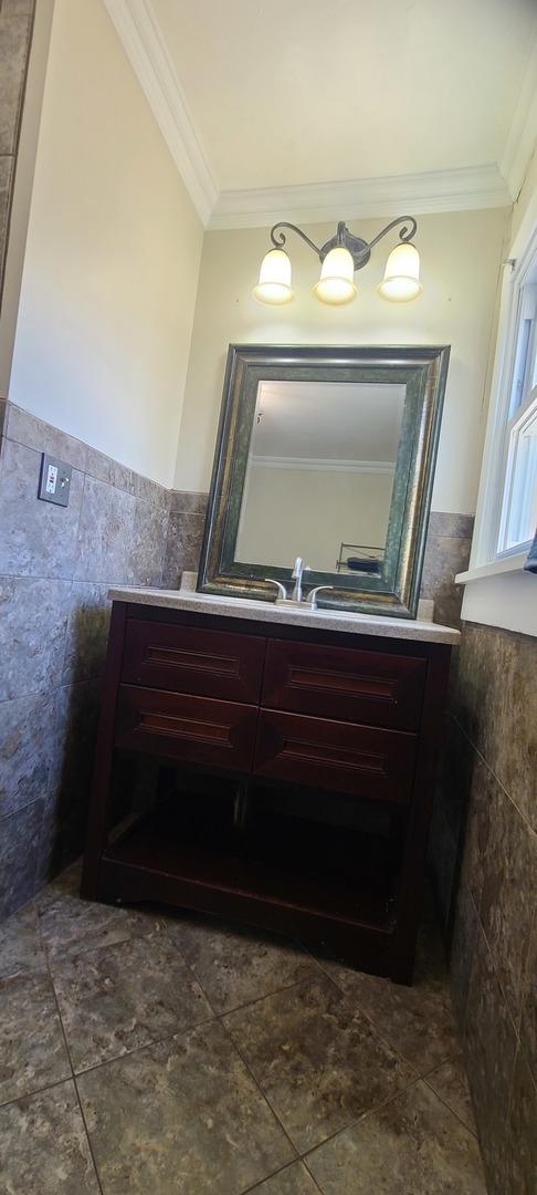 bathroom with vanity, ornamental molding, and tile walls