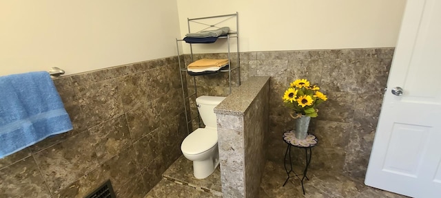bathroom with wainscoting, tile walls, and toilet