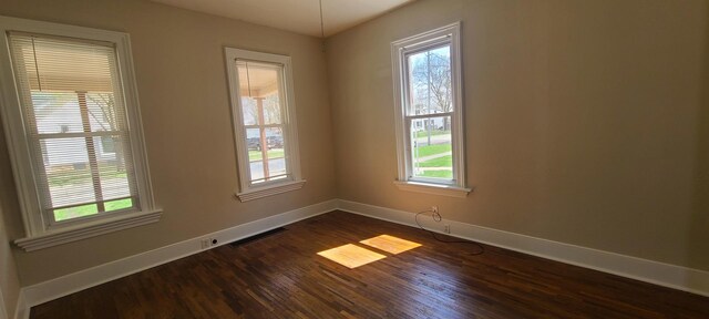 unfurnished room with dark wood-type flooring, visible vents, and baseboards