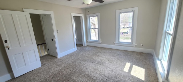 unfurnished bedroom with baseboards, multiple windows, carpet flooring, and a ceiling fan