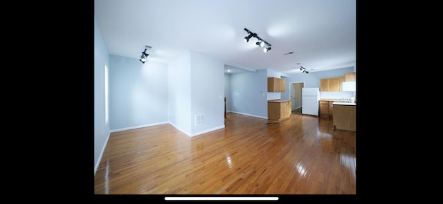 unfurnished living room with rail lighting, baseboards, wood finished floors, and visible vents