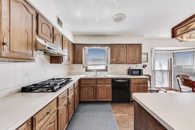 kitchen with visible vents, a sink, black appliances, light wood finished floors, and under cabinet range hood