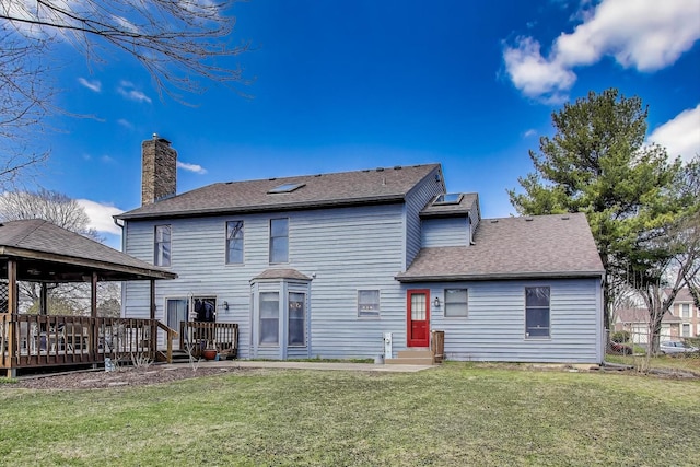 back of house with a lawn, a chimney, a shingled roof, and a wooden deck
