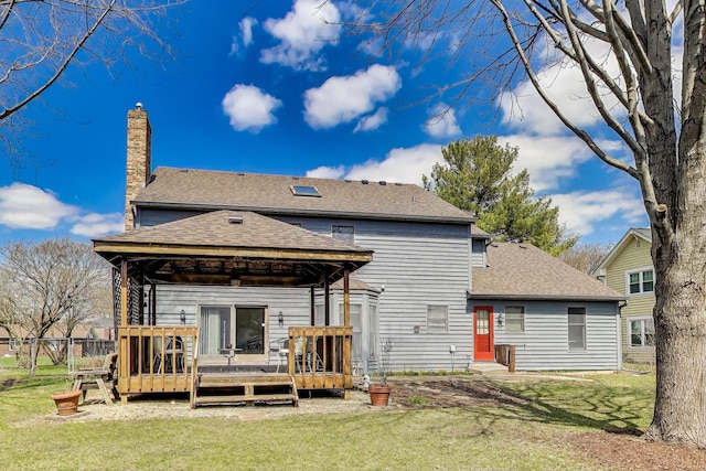 rear view of house featuring a chimney, a deck, a gazebo, a yard, and a shingled roof