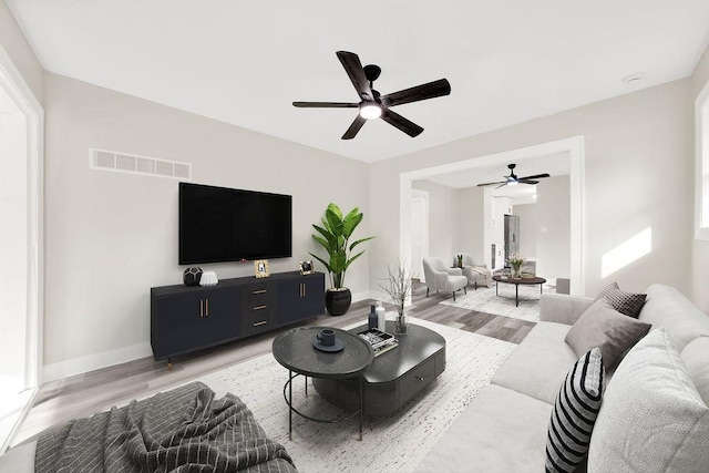 living room with visible vents, baseboards, a ceiling fan, and light wood-style flooring