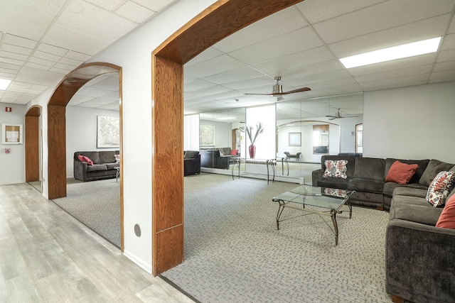 living room with arched walkways, a ceiling fan, carpet, wood finished floors, and a drop ceiling