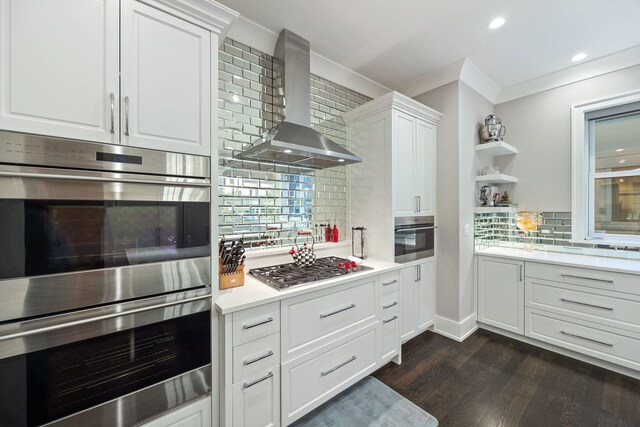 kitchen featuring dark wood-style flooring, light countertops, wall chimney exhaust hood, decorative backsplash, and appliances with stainless steel finishes