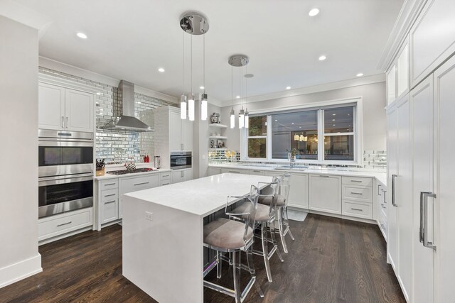 kitchen with tasteful backsplash, light countertops, white cabinets, stainless steel double oven, and wall chimney exhaust hood