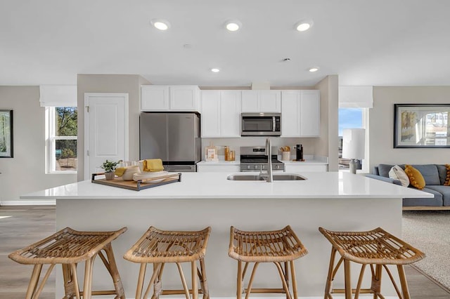 kitchen with white cabinetry, appliances with stainless steel finishes, light countertops, a sink, and open floor plan