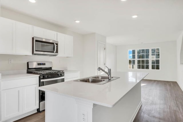 kitchen featuring a sink, appliances with stainless steel finishes, dark wood-style floors, white cabinetry, and a center island with sink