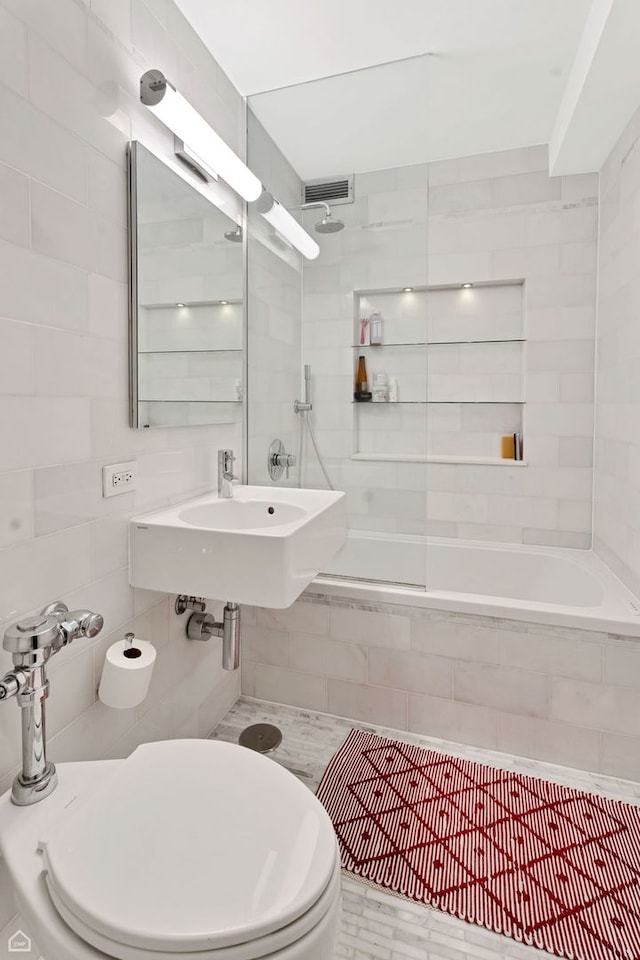 bathroom featuring toilet, visible vents, tiled shower / bath combo, tile walls, and a sink