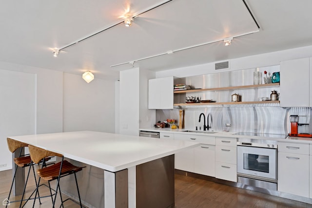 kitchen with track lighting, open shelves, a kitchen island, oven, and a sink