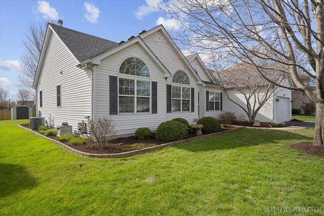 ranch-style home with a shingled roof, central air condition unit, a storage unit, a front yard, and a garage