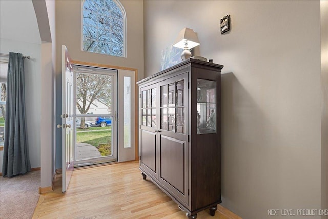 entryway with light wood-style flooring, baseboards, and a high ceiling
