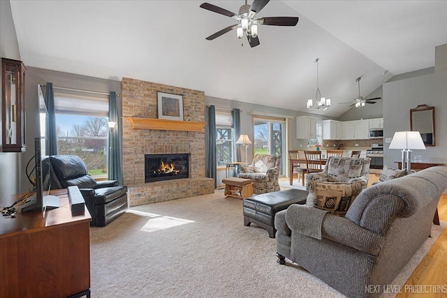living room featuring high vaulted ceiling, a brick fireplace, light colored carpet, and ceiling fan with notable chandelier