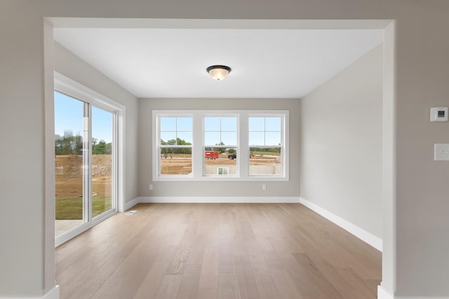 unfurnished room featuring baseboards, light wood-style flooring, and a healthy amount of sunlight