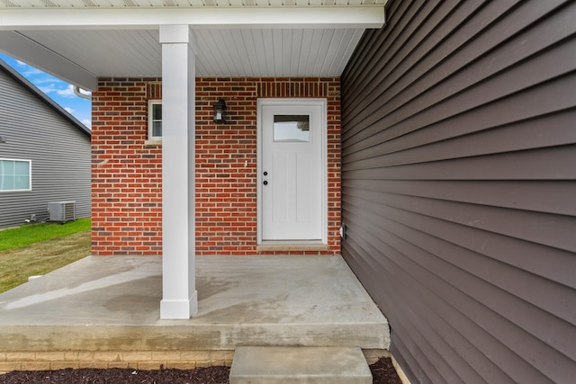 property entrance with a porch, brick siding, and central AC