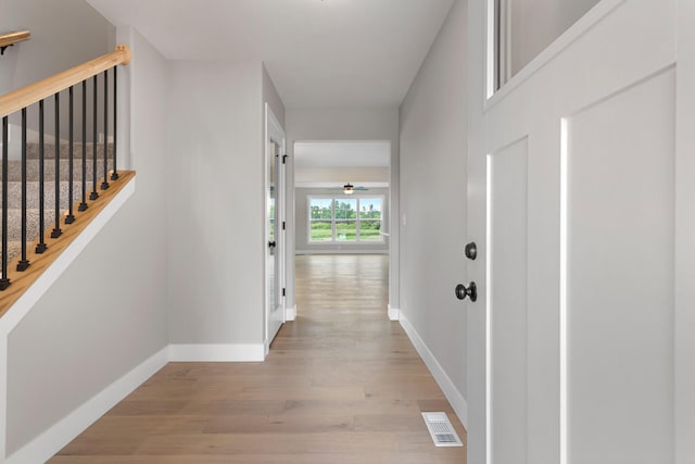 hall featuring light wood-style floors, baseboards, visible vents, and stairway