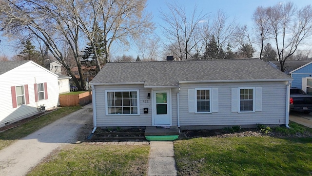view of front facade with roof with shingles, driveway, and a front yard