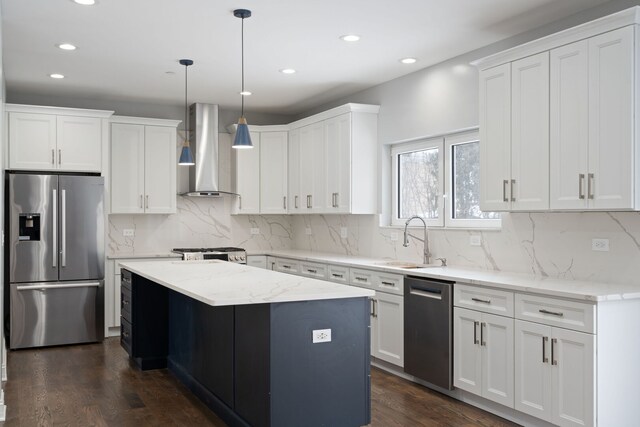kitchen with wall chimney range hood, recessed lighting, a kitchen island, stainless steel appliances, and a sink
