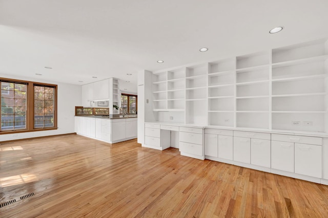 unfurnished living room with light wood-style floors, recessed lighting, a desk, and built in shelves