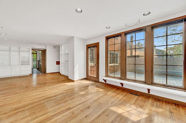 empty room featuring healthy amount of natural light, baseboards, light wood-type flooring, recessed lighting, and built in shelves