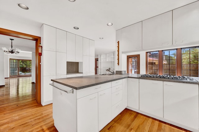 kitchen with a sink, light wood-style floors, stainless steel gas stovetop, a chandelier, and white cabinets